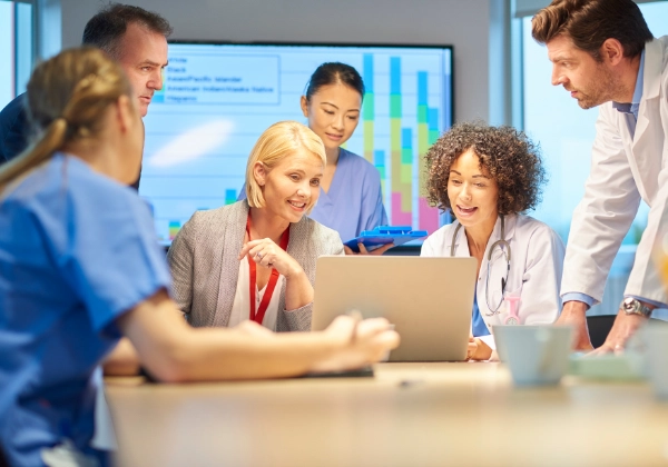 Hospital team with healthcare professionals and business representatives collaborating with a laptop.